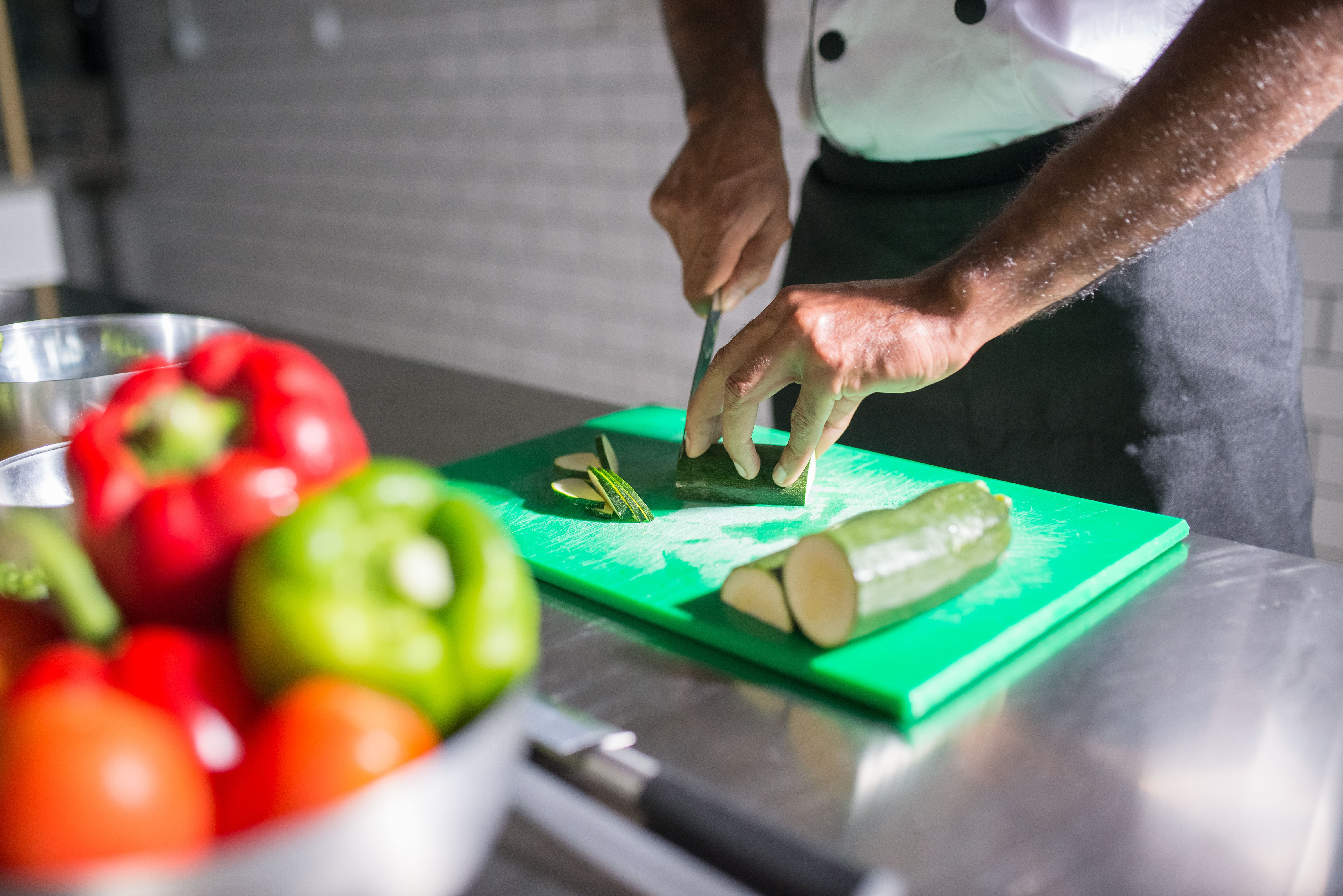 Chef slicing fresh zucchini beside other vegetables in a professional kitchen, highlighting fresh and responsible food preparation.