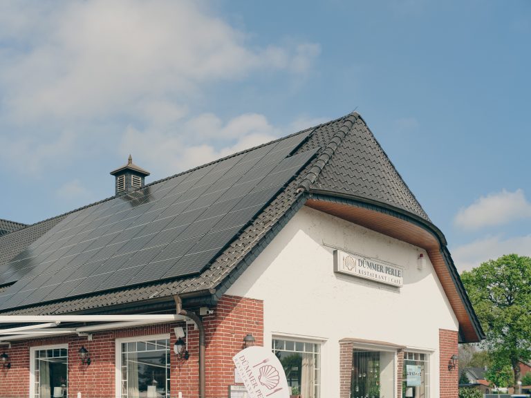 Red brick commercial building with rooftop solar panels under a clear blue sky, illustrating a restaurant's renewable-energy commitment.